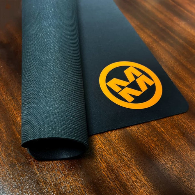 A black deluxe fabric top counter mat with a textured finish and an orange logo.