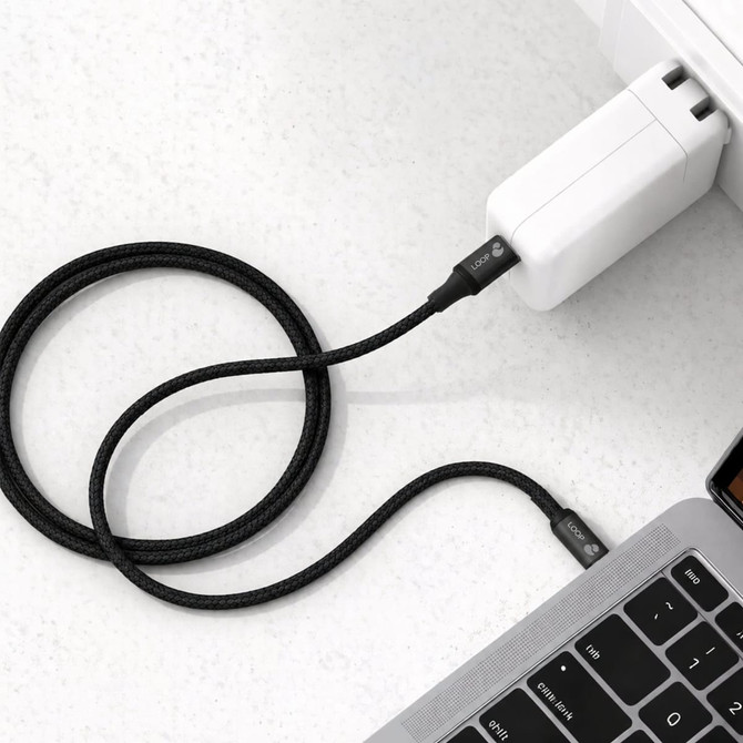 A black braided charging cable connected to a white power adapter and a laptop. It features a logo on the cable.