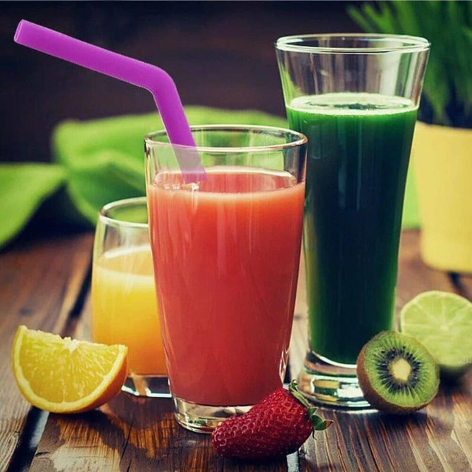 A set of drinks in glasses featuring a purple reusable silicone straw, alongside vibrant fruit and a green beverage.