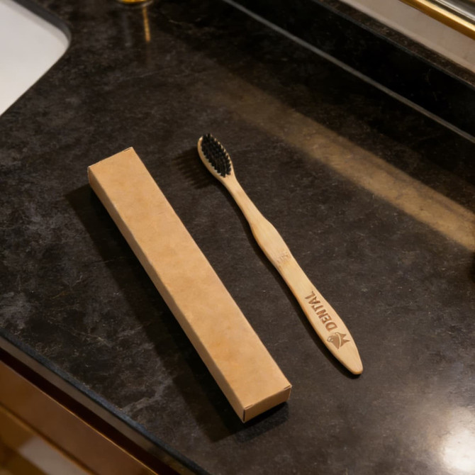 A large wavy handle toothbrush with a wooden handle and black bristles, beside a rectangular brown packaging on a dark countertop.