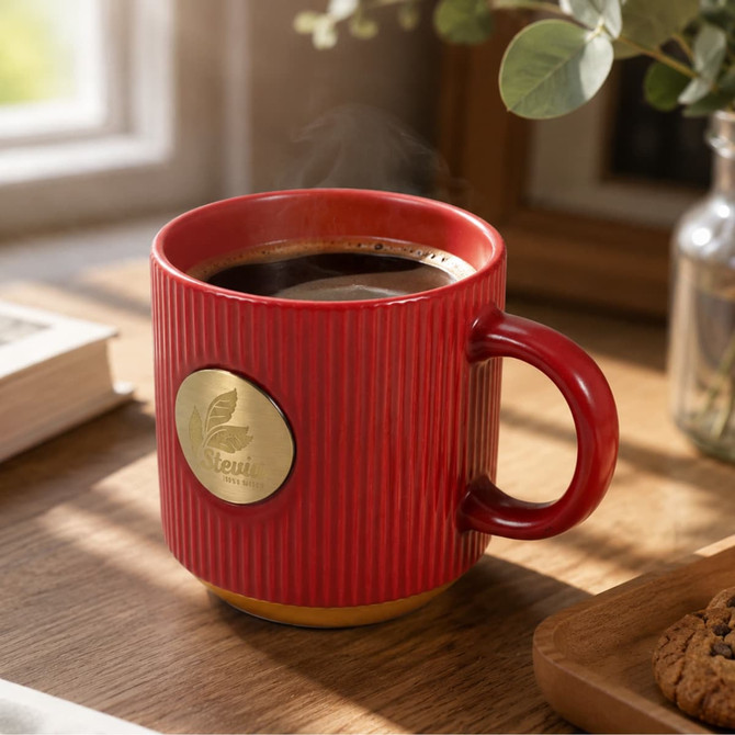A red ceramic coffee mug with a bronze medal, filled with coffee, sits on a wooden surface near a plant and cookie.