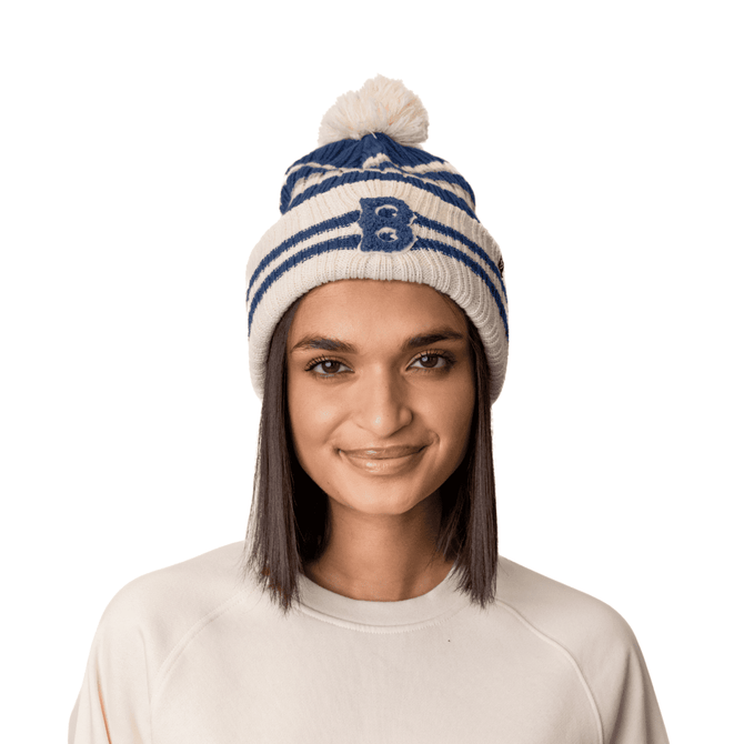 A beanie hat in white and navy, featuring a pom pom on top and a logo, worn by a model.