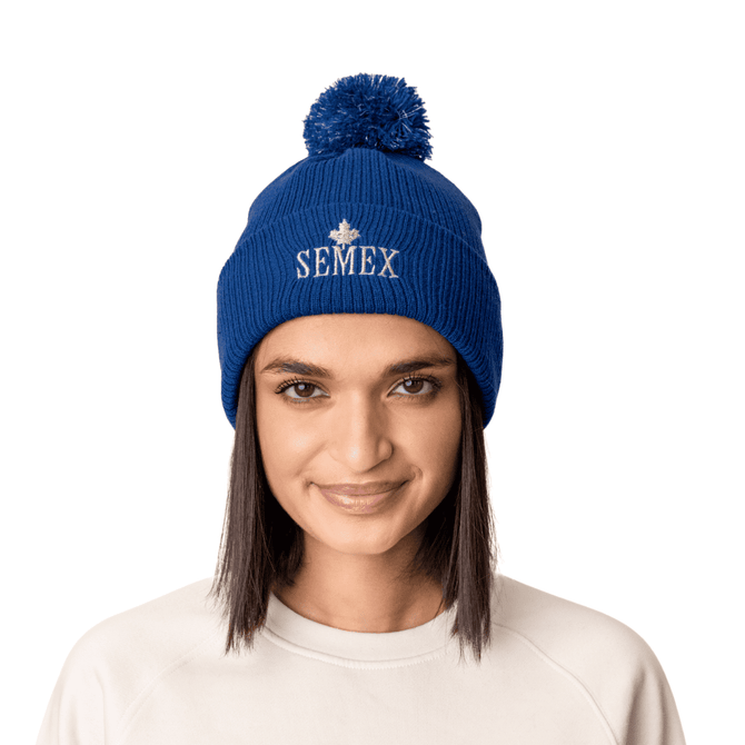 A blue beanie hat with a pom pom on top, featuring a logo on the front.