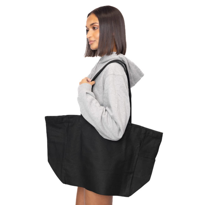 A woman holds a large black canvas tote bag over her shoulder, featuring a simple design and sturdy handles.