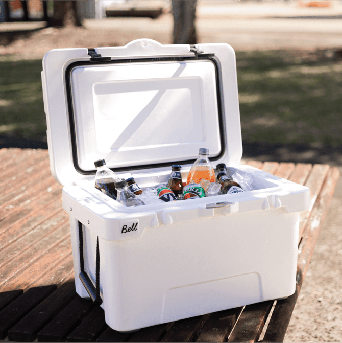 A white cooler box opened to reveal assorted drinks, including bottles and cans, resting on a wooden surface.
