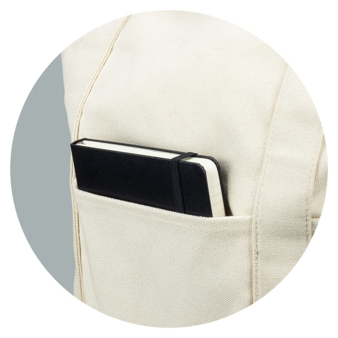 A cream canvas tote bag with a black notebook tucked into a side pocket. The bag features a logo.