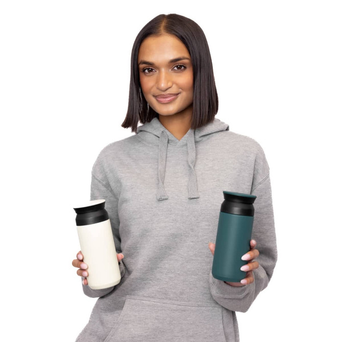 A drink bottle in white and teal, featuring a logo, held by a person in a grey hoodie.