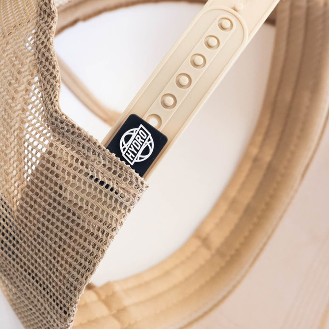 A beige cap featuring a mesh back and a logo on the side, highlighting its headwear design.