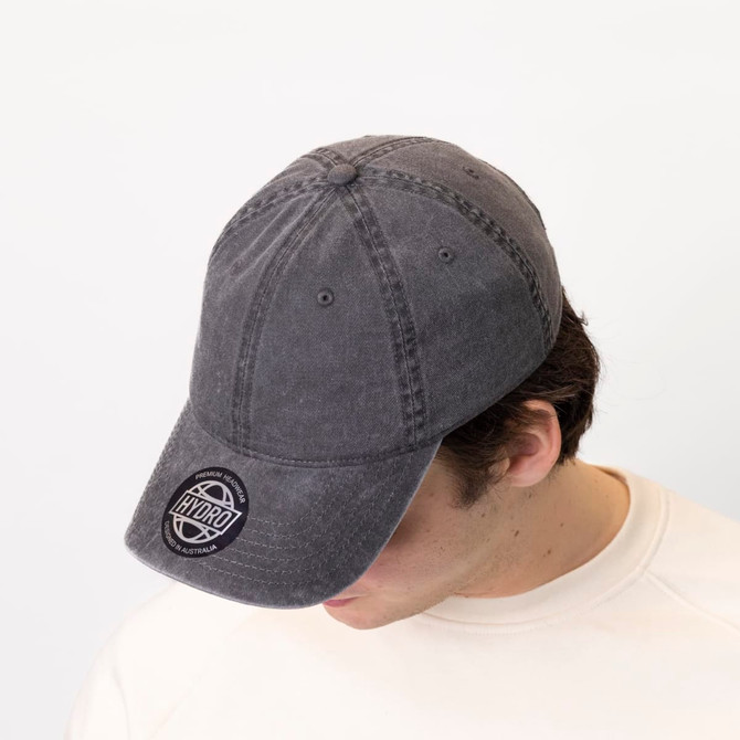 A grey 6-panel chino cotton twill cap featuring a front logo, worn by a person with their head down.