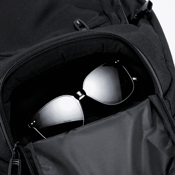 A black backpack with a zippered pocket containing a pair of dark sunglasses inside.