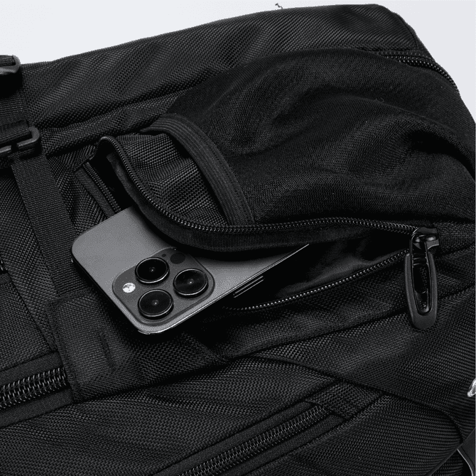 A black Eiger backpack with a smartphone tucked in a zippered pocket. The bag has a textured surface and features a logo.