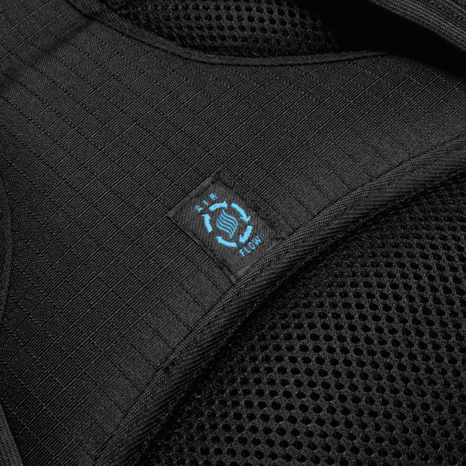 A close-up of a black backpack strap with mesh fabric and a blue logo.