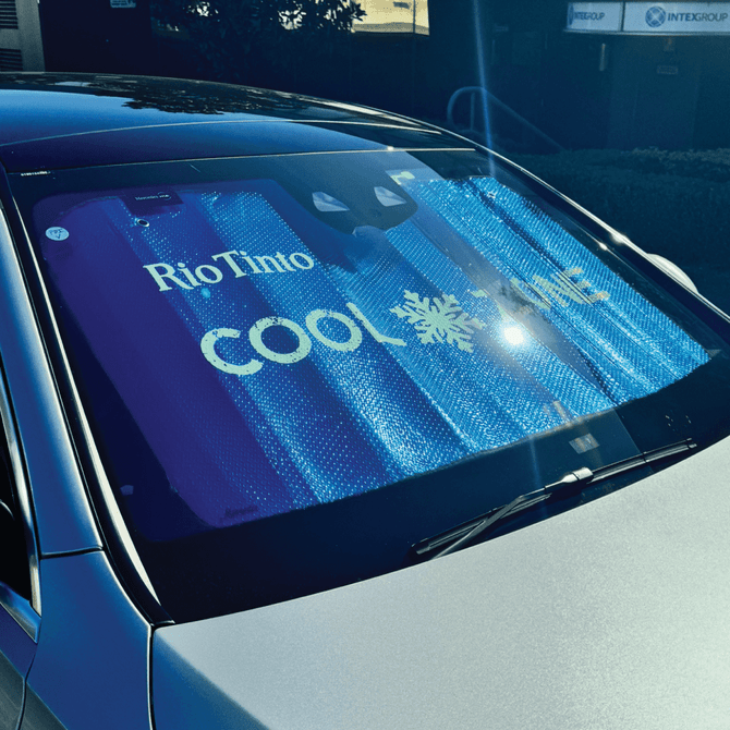 A foldable car sunshade in blue with branding, placed on the windshield of a silver car.