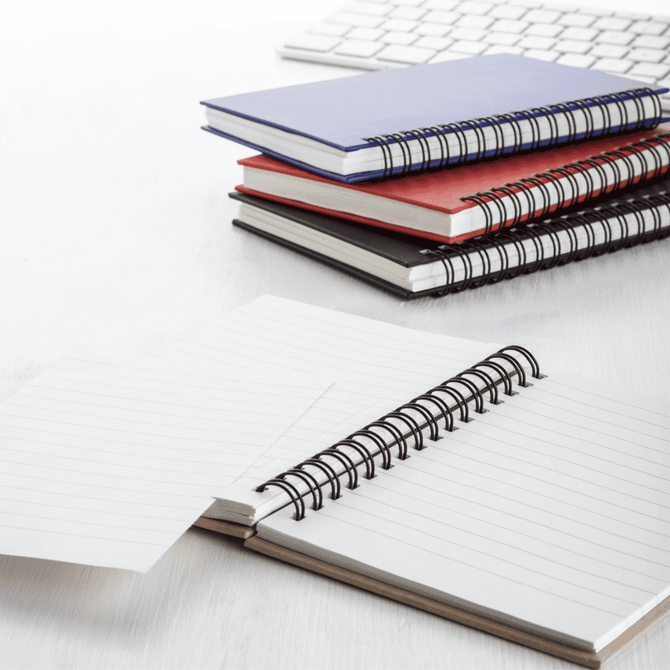 A stack of spiral-bound notebooks in blue, red, black, and white, with one opened to reveal lined pages.