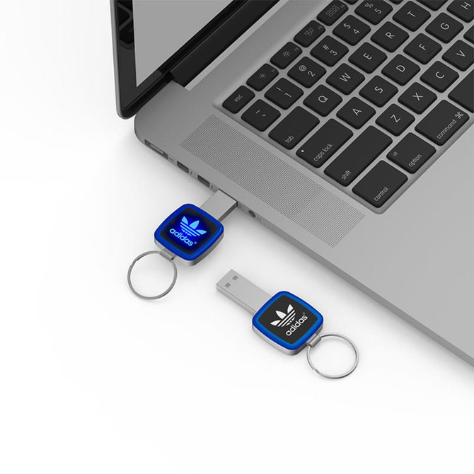 A blue LED USB flash drive is connected to a laptop, featuring a keyring attachment and a logo.