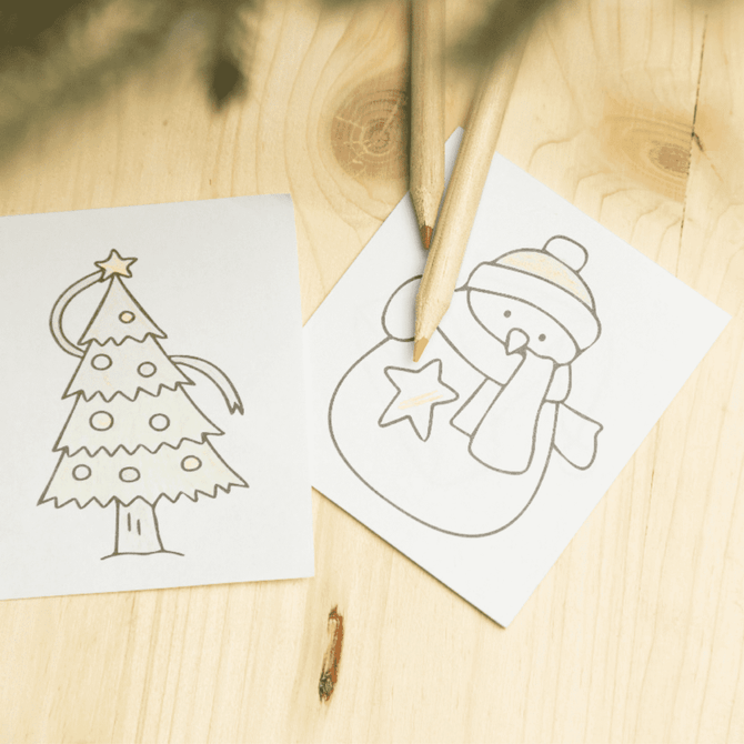 A custom colouring set with two outlined images—a Christmas tree and a snowman—accompanied by yellow and wood-coloured pencils.