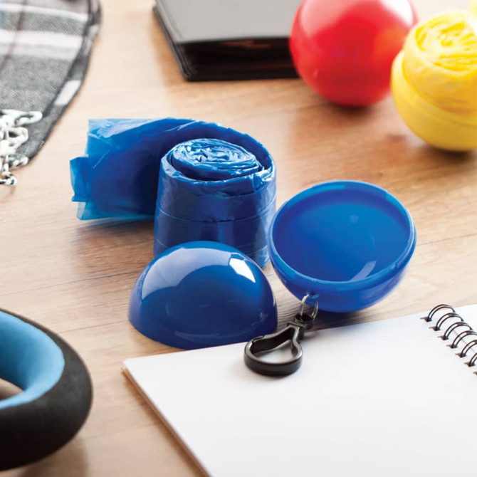 A blue keyring featuring a compact, rolled-up poncho and a snap closure, surrounded by colourful items on a table.