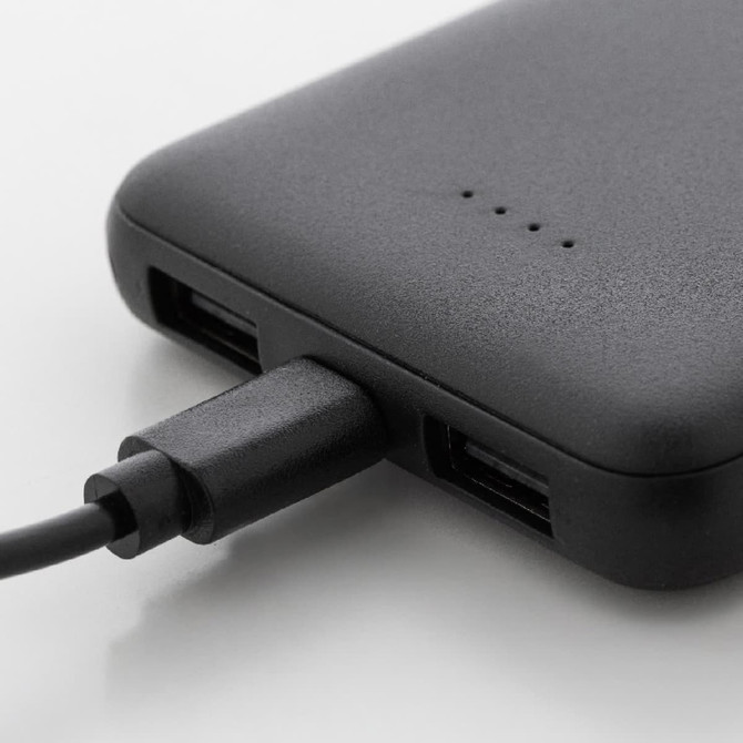 A black power bank with USB ports and a charging cable connected, made from recycled ABS material.