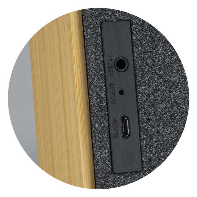 A close-up of the back of a grey and wooden Bluetooth speaker, featuring ports for audio and charging.
