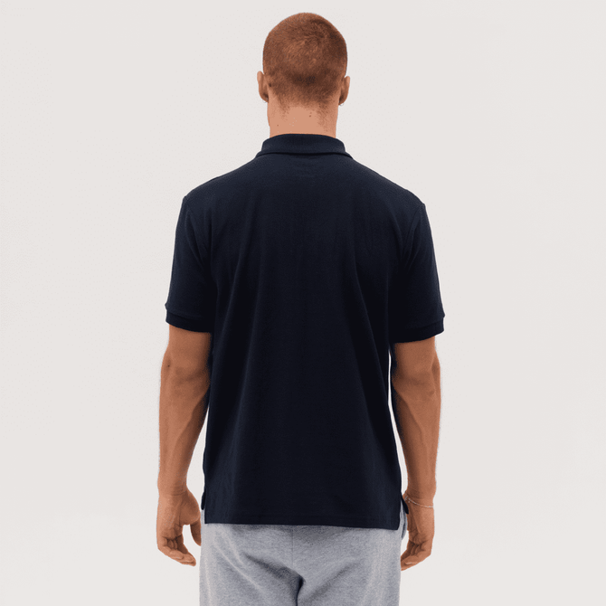 A navy polo shirt with a collar, viewed from the back. The model has short hair and is wearing grey shorts.