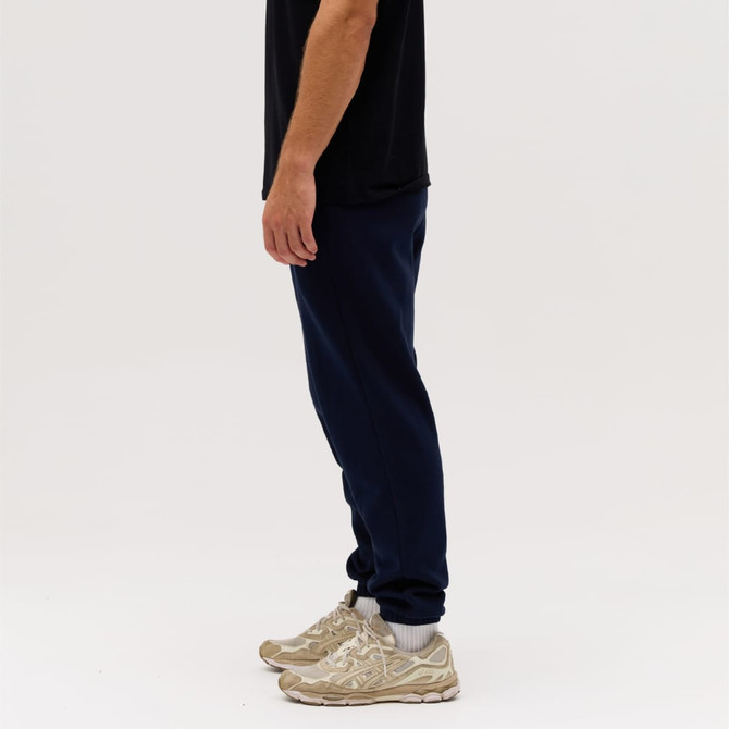 Navy track pants featured on a person, paired with beige sneakers, against a plain white background.