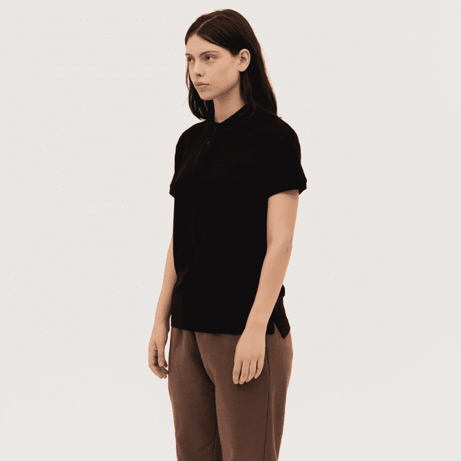 A black women's polo shirt with a classic collar and short sleeves. The model is standing in a neutral pose.