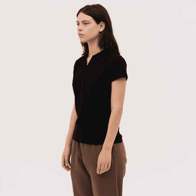 A black women's polo shirt with a zip front and short sleeves, paired with light brown trousers.
