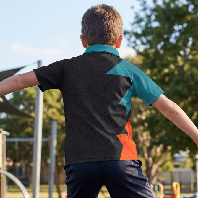 A boy wearing a black, teal, and orange custom youth active polo shirt in an outdoor playground setting.