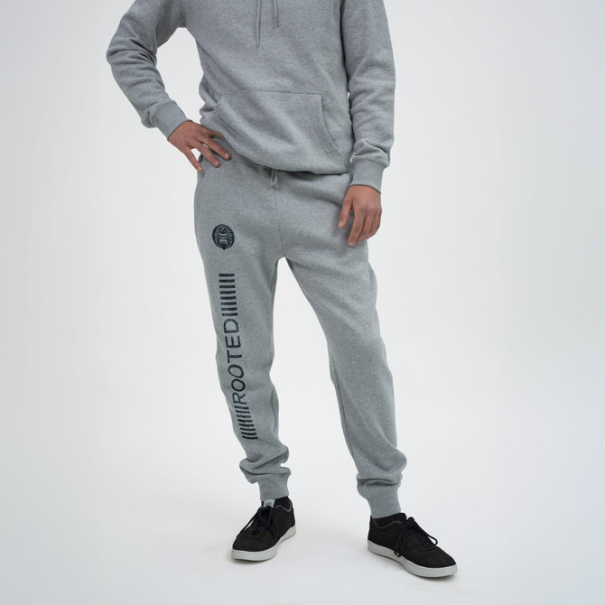 A model wearing grey unisex sweatpants with a logo and text along the side, paired with black shoes.
