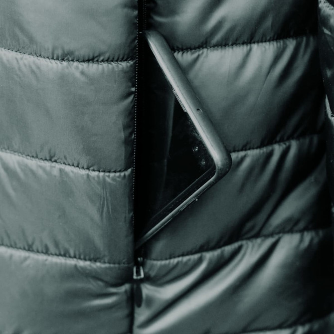 A puffer jacket with a zippered pocket, containing a smartphone, in a dark colour.