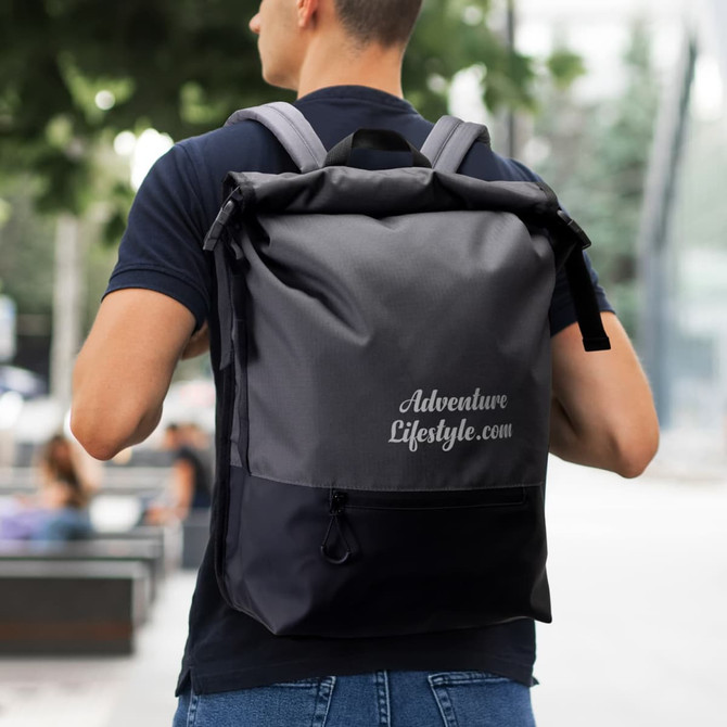 A person wearing a grey and black Fjord Backpack, with a logo on the back, standing outdoors.