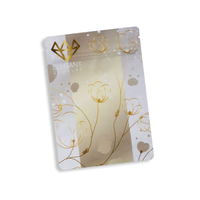 A small, metallic stand-up pouch in silver and gold, featuring floral designs and a logo.
