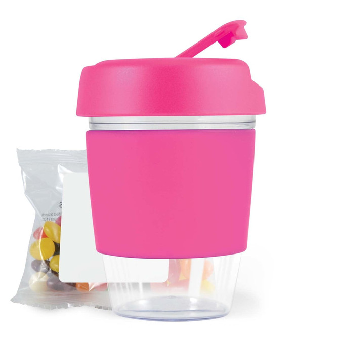 A pink reusable coffee cup with a clear base and a lid, accompanied by a bag of colorful jelly beans.