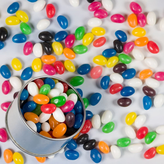 A silver round tin filled with assorted colour mini jelly beans, surrounded by more jelly beans in various colours.