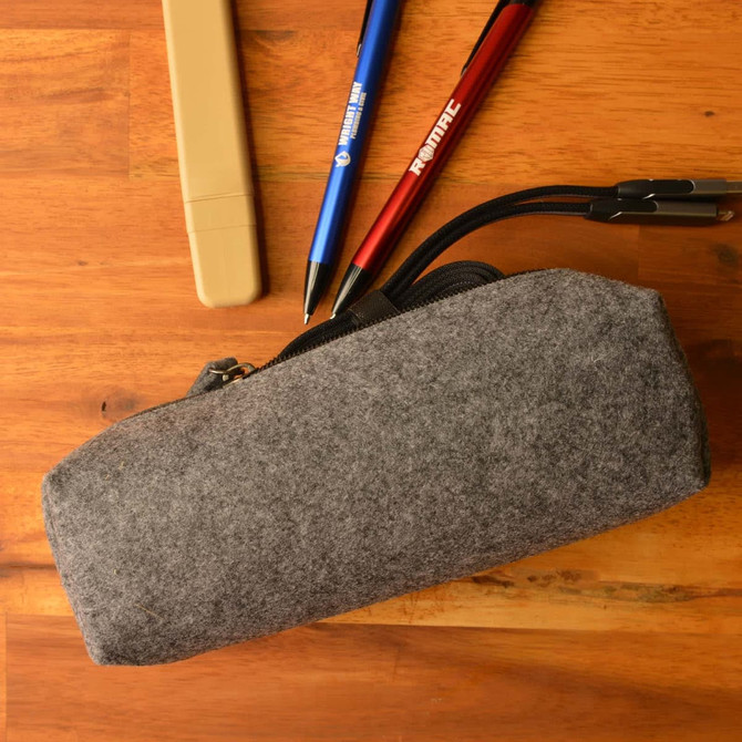 A gray felt utility case with a zipper, accompanied by pens and a highlighter placed on a wooden surface.