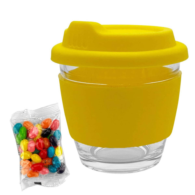 A yellow glass coffee cup with a silicone sleeve and lid, alongside a packet of colourful jelly beans.