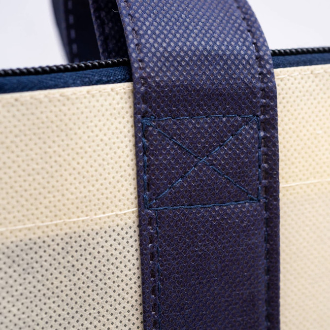 A close-up of a non-woven zipped shopping bag featuring navy handles and a beige body, with stitching details visible.