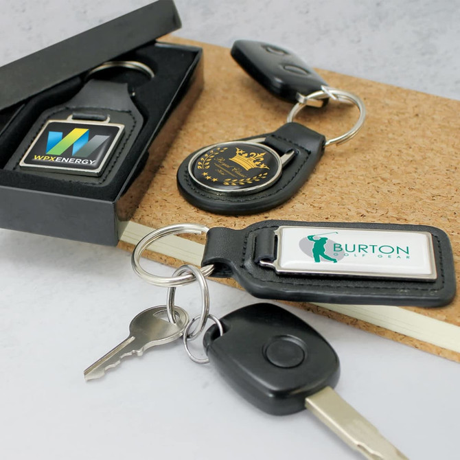 A round leather key ring in black with a metal ring, displayed with additional key rings in a box.