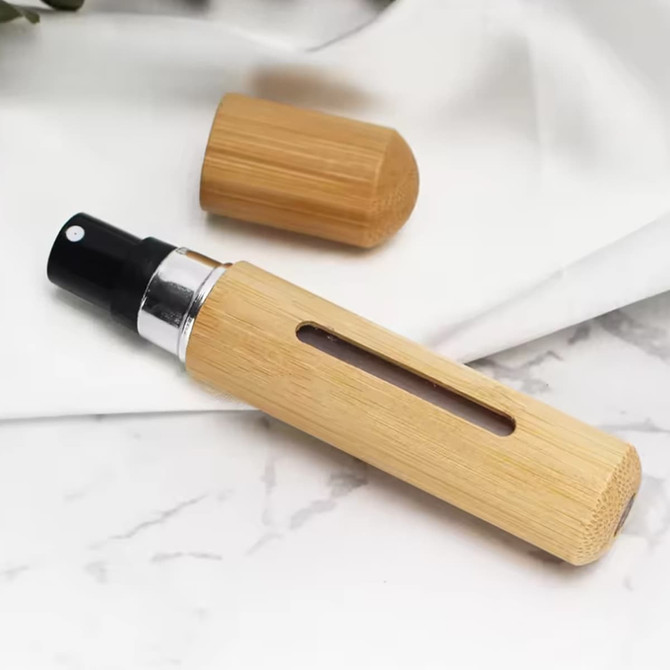 A bamboo atomiser with a black spray nozzle, featuring a clear section and a removable cap, resting on a white surface.