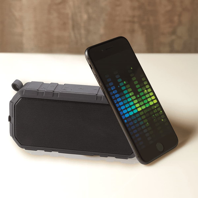 A grey outdoor waterproof Bluetooth speaker placed next to a smartphone displaying a visual equaliser.