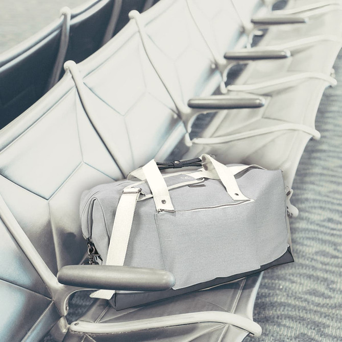 A grey duffel bag with white straps rests on a seating area, featuring a logo on the side.