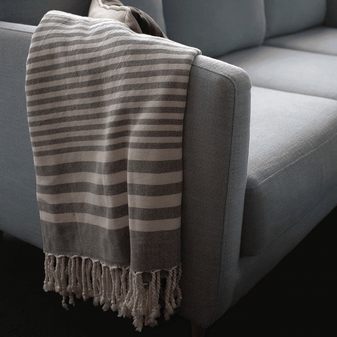 A light grey and white striped throw blanket with tassels draped over the arm of a blue sofa.