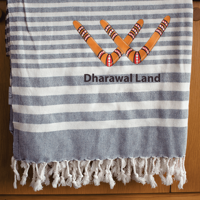 A blue and white striped throw blanket with a fringed edge and a logo featuring boomerangs and the text "Dharawal Land."