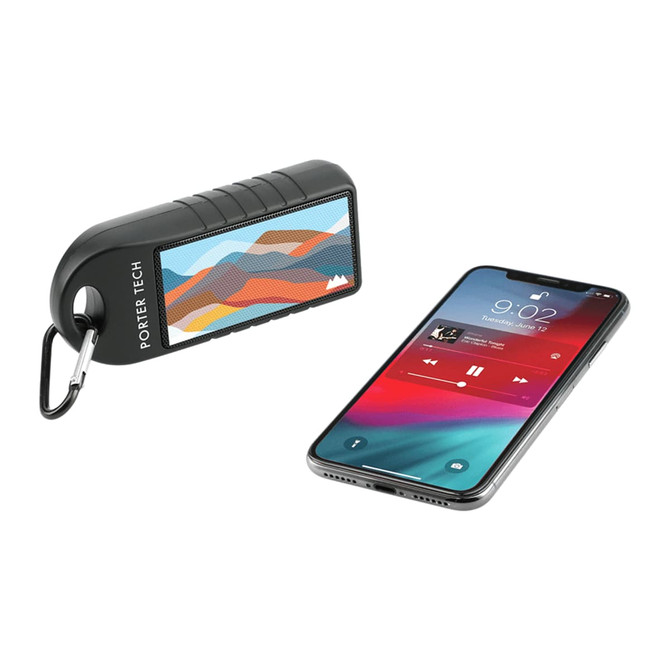 A black Bluetooth speaker with a mountain design beside a smartphone displaying music playback.