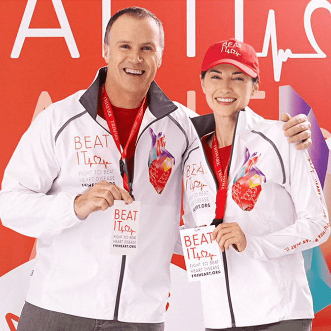 Two individuals wearing white Egmont Packable Jackets with a logo, posing with medals and a red hat.
