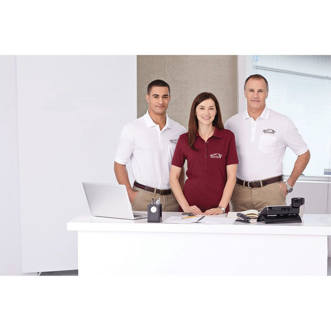 Three individuals are wearing Crandall Short Sleeve Polo shirts in white and burgundy, featuring a logo. They are at a desk with office supplies.