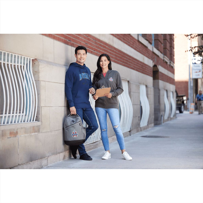 A man in a navy hoodie and a woman in a grey hoodie pose casually on a street corner, both with backpacks.