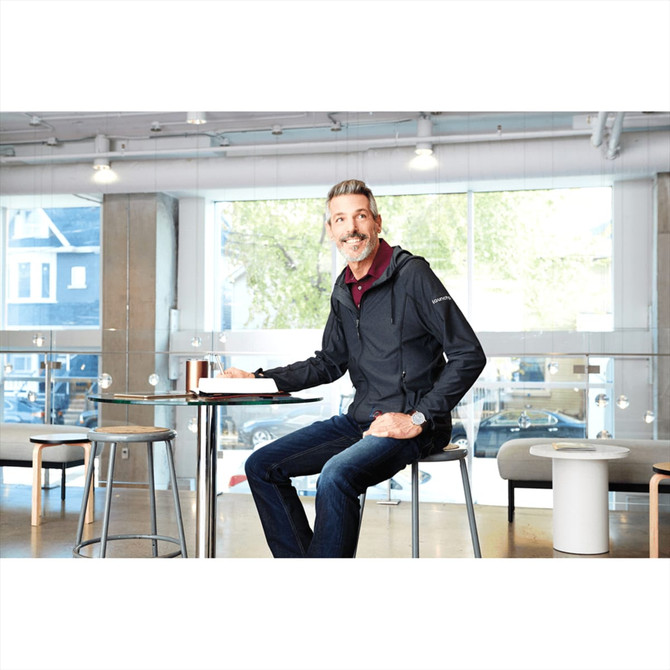 A man in a black Kaiser Knit Jacket sits at a table, surrounded by a modern interior setting.