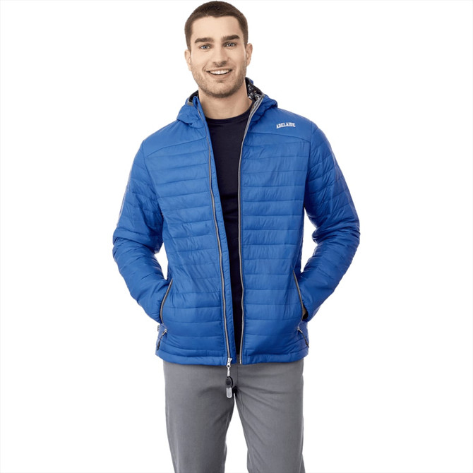 A man wearing a blue packable puffer jacket with a hood, featuring a logo. The jacket is zipped and has side pockets.