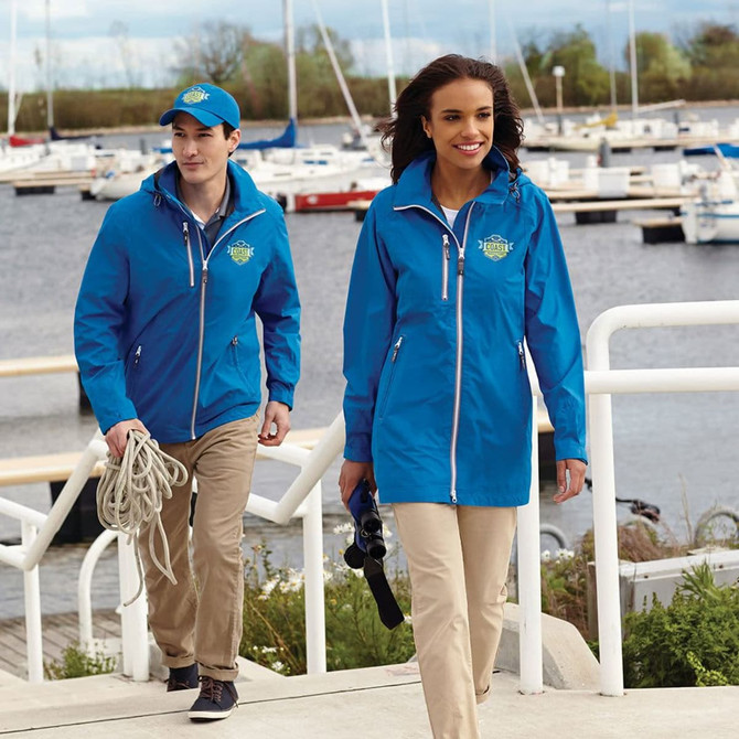A blue rain jacket worn by a woman, paired with a blue cap and beige trousers, near a marina.